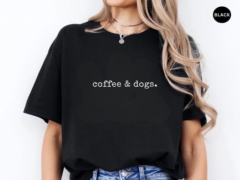 May include: Black t-shirt with the text "coffee & dogs." in a white, simple font. The shirt is a basic crew neck style. The model is wearing blue jeans.