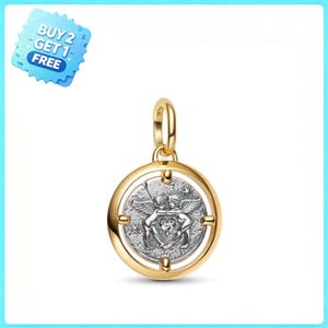 Puede incluir: Un colgante circular con un marco exterior dorado y un disco central plateado. El disco central representa a dos figuras aladas abrazadas, con un pequeño corazón entre ellas. Se observa una etiqueta azul con el texto BUY 2 GET 1 FREE.