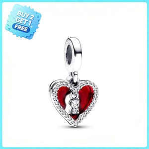 Puede incluir: Un charm de plata en forma de corazón con un esmalte rojo vibrante, un borde de pequeñas piedras transparentes y un recorte central en forma de cerradura que contiene una piedra brillante. Incluye una anilla superior para su sujeción.