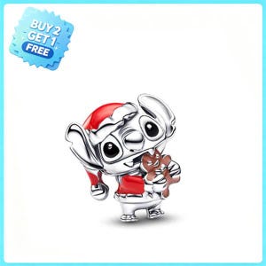 Puede incluir: Un charm de plata que muestra un personaje con gorro de Papá Noel rojo y abrigo rojo, sosteniendo un hombre de jengibre marrón. Una insignia azul en forma de estrella muestra el texto BUY 2 GET 1 FREE. El charm tiene detalles en esmalte negro.