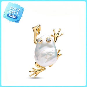 Pode incluir: Um pingente de sapo em tom dourado com um corpo formado por uma grande pérola barroca branca irregular. O sapo tem membros dourados finos e duas pequenas pedras claras de corte redondo como olhos. Um emblema azul exibe BUY 2 GET 1 FREE.