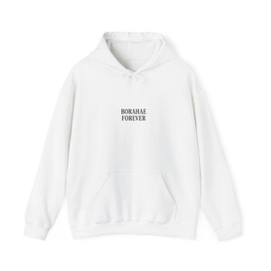 Könnte beinhalten: Weißer Kapuzenpullover mit Fronttasche und Kordelzugkapuze. Der Text "BORAHAE FOREVER" ist in Schwarz auf der Vorderseite aufgedruckt. Der Hoodie ist aus weichem Material.
