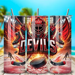 May include: A stainless steel tumbler with a hockey design. The design features a red hockey goalie mask, crossed hockey sticks, and the word "DEVILS" in white and red. A hockey puck and ice skates are also visible.