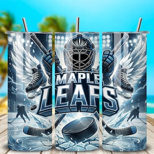 May include: A stainless steel tumbler featuring a hockey-themed design. The design includes a goalie mask, hockey skates, and the words "MAPLE LEAFS" in a bold, blue font. The background depicts a hockey rink with players and a puck.