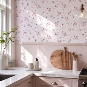 May include: A kitchen wall featuring light pink wallpaper with a repeating pattern of small purple and pink flowers, green leaves, and tiny butterflies. Below the wallpaper is light pink wainscoting, a white marble countertop, and wooden boards.