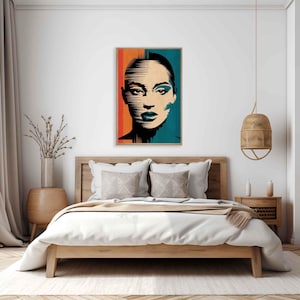 Può includere: Una stampa artistica incorniciata con un ritratto stilizzato del volto di una donna. L'opera è divisa verticalmente, con un lato arancione e rosso e l'altro turchese. Il volto della donna è reso in bianco e nero con accenti turchesi e blu.