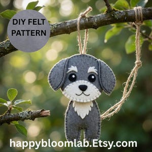 Könnte beinhalten: Graues Filzhunde-Ornament mit weißen Akzenten, das an einem Ast hängt. Das Ornament hat große, schlaffe Ohren und einen freundlichen Gesichtsausdruck. Der Text "DIY FELT PATTERN" befindet sich in einem grauen Kreis. Der Etsy-Shop-Name "happybloomlab.Etsy.com" steht unten.