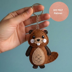 May include: A handmade felt beaver keychain in shades of brown, tan, and black. The beaver has white accents, a small tail, and a metal keyring. The text "DIY FELT Pattren" is in a peach circle in the background.