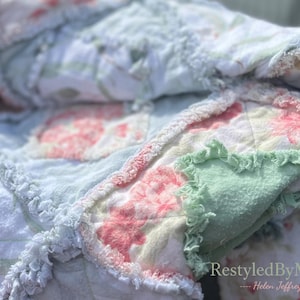 May include: Close-up of a handmade quilt with a floral pattern in shades of pink, green, and white. The quilt has a ruffled edge and a soft, textured appearance. The text "RestyledByMe" and "Helen Jeffrey" are visible.