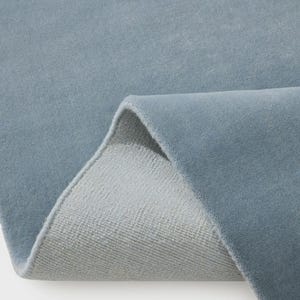 Sky blue minimalist plush area rug in modern living room with wooden floor and chair, soft solid carpet decor