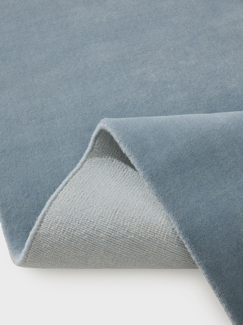 Sky blue minimalist plush area rug in modern living room with wooden floor and chair, soft solid carpet decor