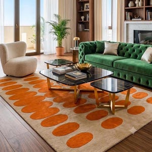 May include: A rectangular area rug featuring a beige base with a repeating pattern of large, rounded orange shapes. The rug is positioned under a set of two black marble-topped coffee tables with gold-toned metal legs in a living room setting.