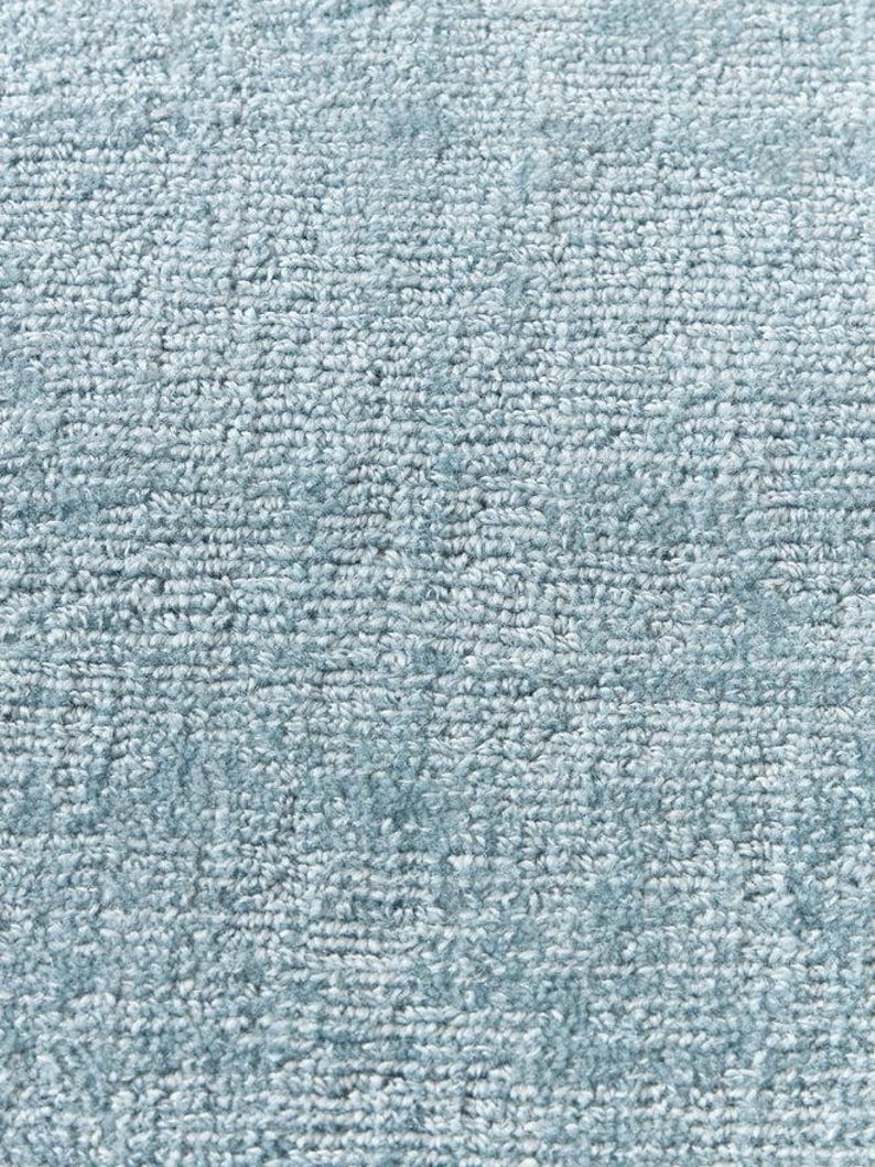 May include: Close-up of a light blue rug with a textured, looped pile. The rug's surface is a consistent color, with subtle variations in tone. The texture appears soft and inviting, suitable for home decor.