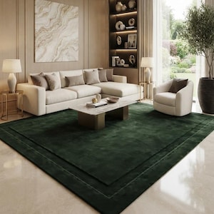 May include: A large rectangular area rug in a deep forest green color with a subtle border detail, positioned on a polished light-colored floor in a living room featuring a cream-colored sectional sofa, a marble coffee table, and an armchair.