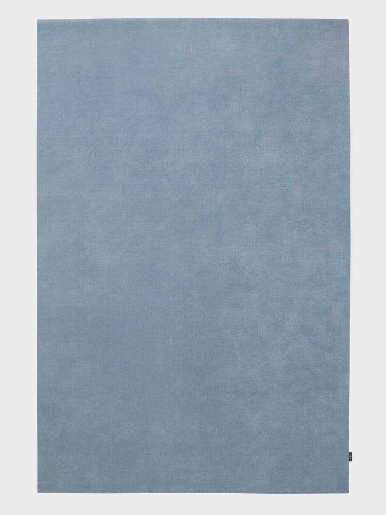 Sky blue minimalist plush area rug in modern living room with wooden floor and chair, soft solid carpet decor