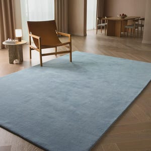 Sky blue minimalist plush area rug in modern living room with wooden floor and chair, soft solid carpet decor