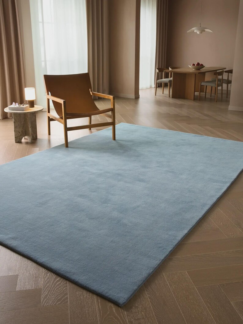 Sky blue minimalist plush area rug in modern living room with wooden floor and chair, soft solid carpet decor