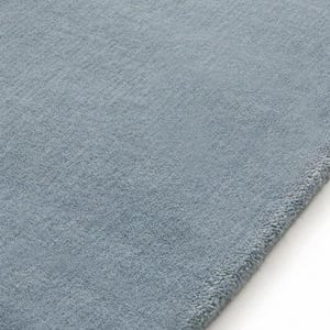 Sky blue minimalist plush area rug in modern living room with wooden floor and chair, soft solid carpet decor