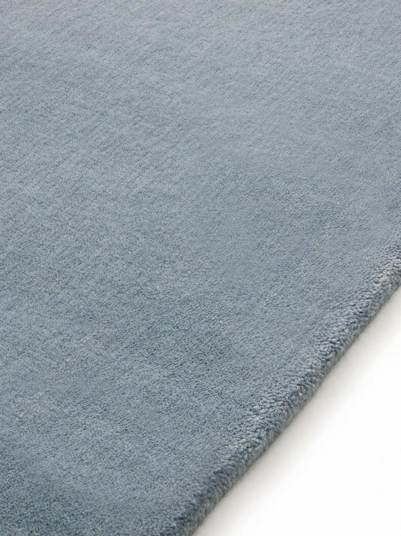 Sky blue minimalist plush area rug in modern living room with wooden floor and chair, soft solid carpet decor