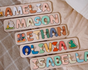 Könnte beinhalten: Holz-Namenspuzzles mit bunten Buchstaben, die "AMELIA", "MASON", "ETHAN", "OLIVIA" und "ISABELLA" buchstabieren. Jedes Puzzle zeigt eine andere Tierillustration. Die Puzzles liegen auf einer hellen Oberfläche.
