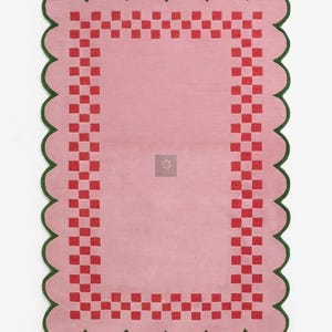 May include: A rectangular pink rug with a scalloped green border. The rug features a red checkered pattern around the edges and a solid pink center. The rug is designed for indoor use.