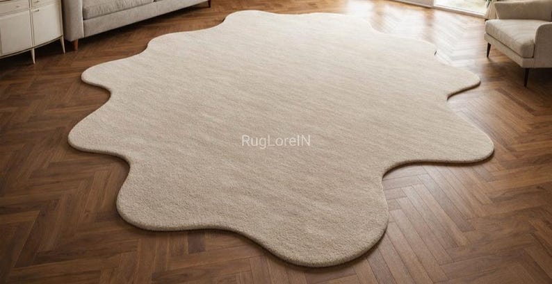 May include: A large, beige, organically shaped area rug. The rug has a soft, textured appearance and is placed on a dark wood floor. The rug's unique shape adds a modern touch to the room's decor. The text "RugLorelN" is visible on the rug.