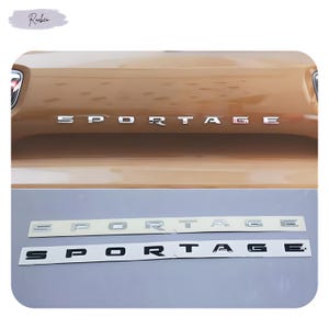 Puede incluir: Primer plano de la parte trasera de un coche con la palabra "SPORTAGE" en letras plateadas. Debajo, se muestran dos juegos de letras "SPORTAGE", uno en plata y otro en negro.