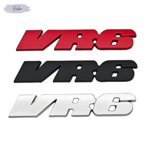 Puede incluir: Tres insignias de emblema VR6 en rojo, negro y plateado. Cada insignia presenta el texto "VR6" en una fuente en negrita y sin serifa. Las insignias rojas y negras tienen un acabado brillante, mientras que la insignia plateada tiene un brillo metálico. Las insignias son probablemente para uso automotriz.