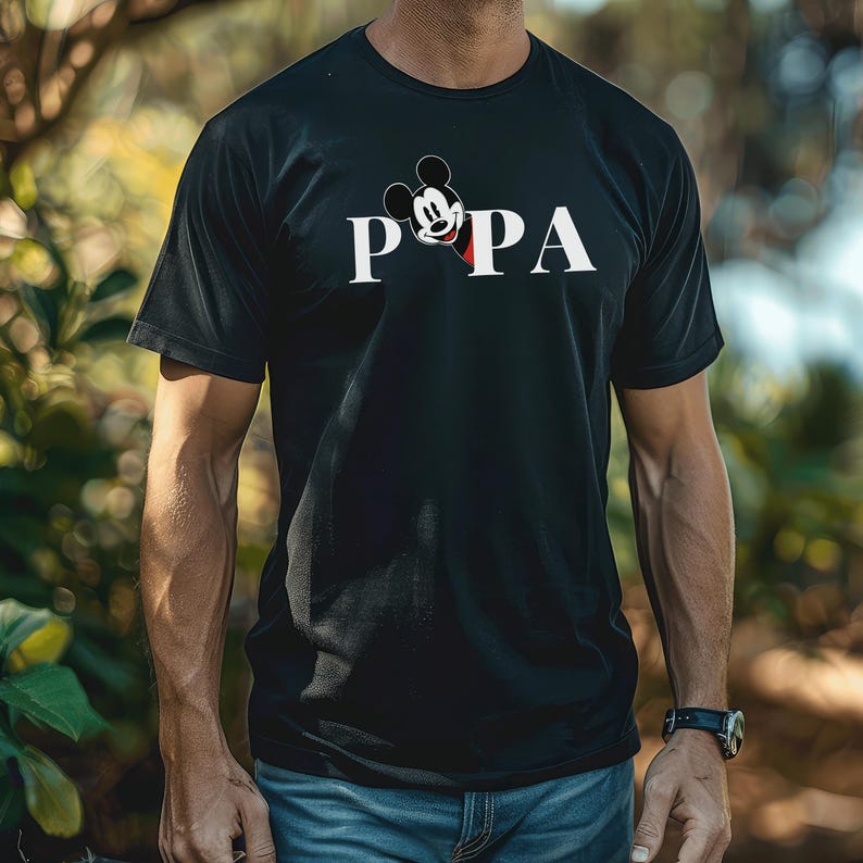 May include: Black t-shirt with the word "PAPA" in white block letters, featuring a Mickey Mouse graphic. The shirt is a crew neck style and is being worn by a person.