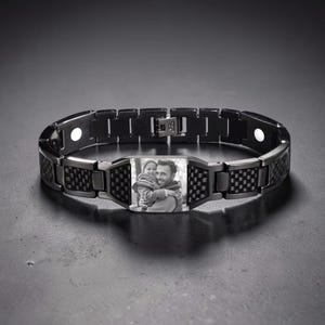 May include: A black link bracelet featuring a central rectangular plate with a black and white photograph of a person holding a child. The bracelet has carbon fiber-style textured accents on the links and small circular magnetic inserts.