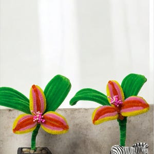 May include: Two decorative floral arrangements. One features a colorful flower in a black pot. The other has a zebra figurine on a colorful base. The flowers have yellow, pink, and red petals with green leaves.