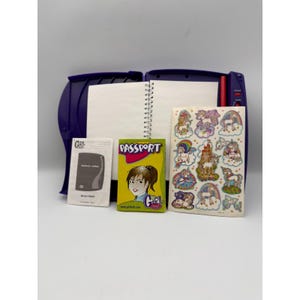 May include: A purple electronic diary with a spiral-bound notebook, a yellow passport booklet labeled Passport Girl Tech, and a sheet of stickers featuring unicorns, rainbows, and a castle. The diary includes a small instruction manual.