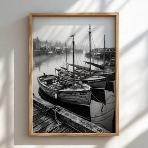 May include: A black and white framed wall art print depicting a harbor scene with several wooden fishing boats moored at a wooden pier. One boat in the foreground is labeled SELKIE WH 102, and another is labeled MAID OF MORAY.