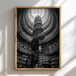 May include: A black and white framed wall art print featuring a central spiral staircase rising through a circular library. The structure is surrounded by multiple levels of curved bookshelves filled with books, topped by a bright skylight.