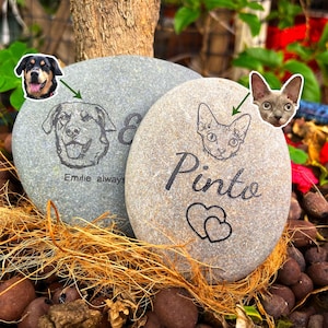 May include: Two engraved stones with pet portraits. One stone features a dog portrait with the text "Emilie always". The other stone has a cat portrait with the name "Pinto" and two hearts.