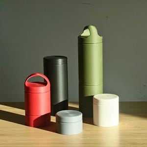 May include: A set of three ceramic mugs with a speckled, matte finish. Each mug features a different color: light blue, cream, and gray. The mugs have a simple, modern design and a comfortable handle.