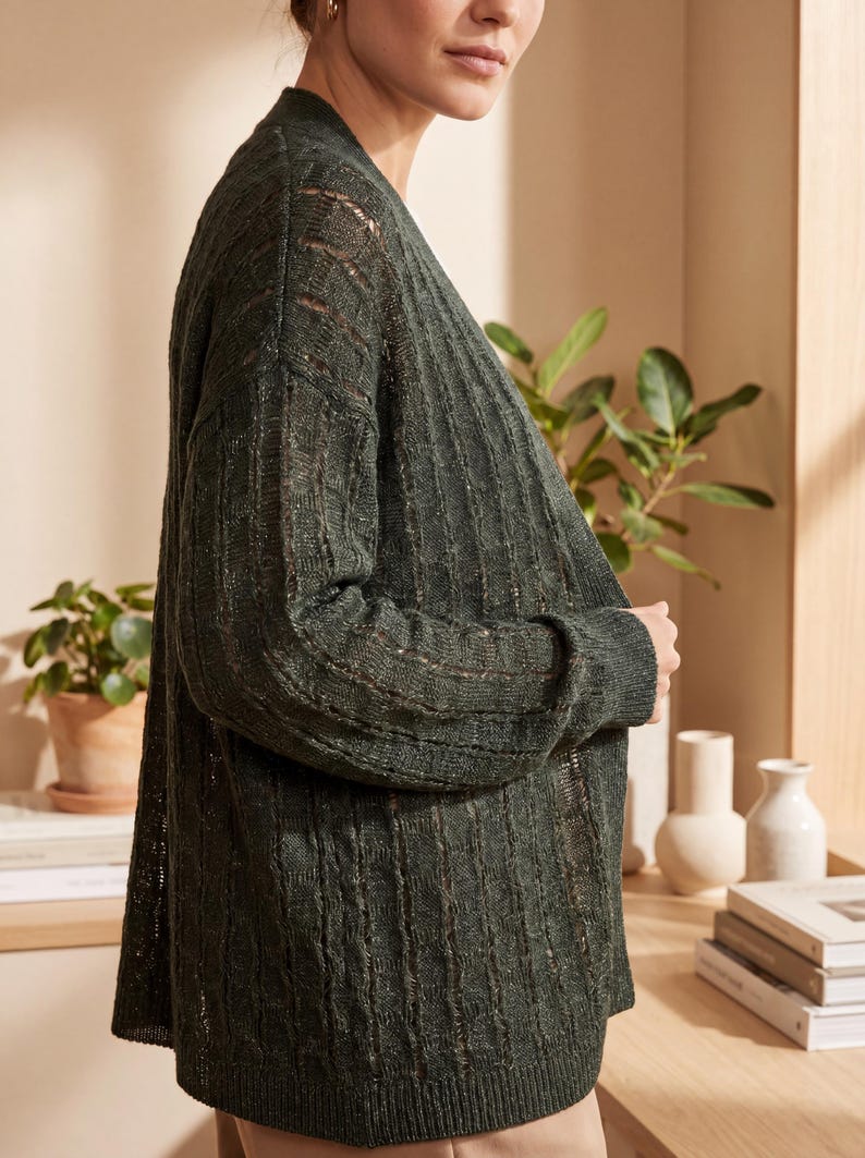 May include: A dark forest green open-front cardigan featuring a vertical ribbed knit pattern with alternating sheer, open-work panels. The garment has long sleeves with ribbed cuffs and a straight hemline, crafted from a lightweight, textured knit fabric.