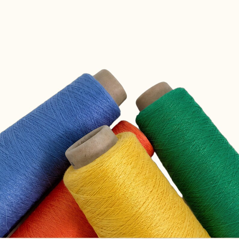 May include: Four industrial spools of thread arranged in a cluster. The spools feature vibrant colors including a deep blue, a bright green, a sunny yellow, and a bold orange. Each spool has a central cardboard core and is tightly wound.