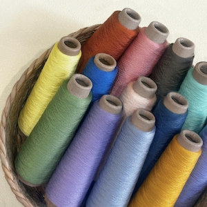May include: A wicker basket filled with colorful spools of thread. The spools are various colors, including yellow, green, blue, purple, and orange. The thread is tightly wound around cardboard cores.