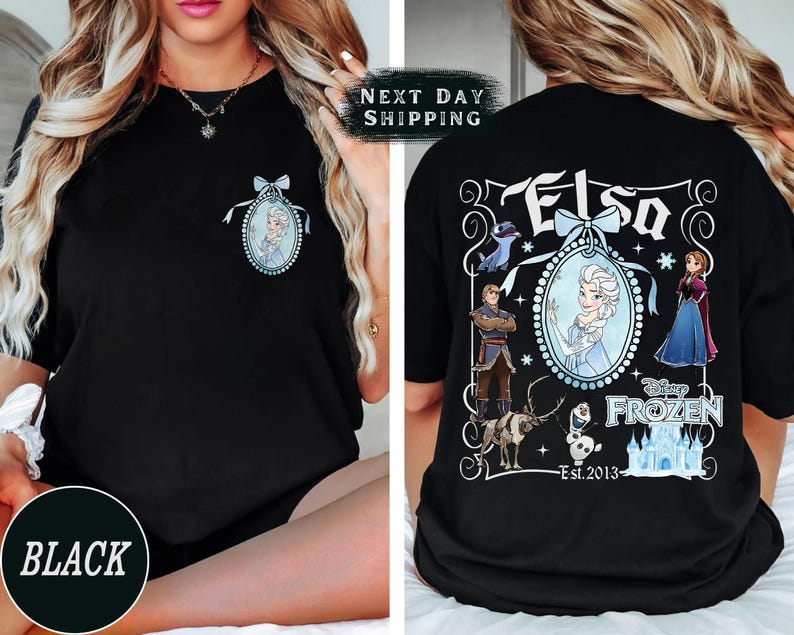 May include: Black t-shirt featuring a front pocket design of Elsa from Disney's Frozen. The back of the shirt displays a larger graphic with Elsa, other characters, and the text "Elsa" and "Disney Frozen Est. 2013".