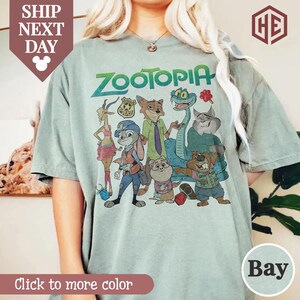 Puede incluir: Camiseta verde claro con la palabra "Zootopia" y personajes de dibujos animados estampados en la parte delantera. La camiseta tiene cuello redondo y mangas cortas. El texto "Click to more color" est&aacute; en la parte inferior.