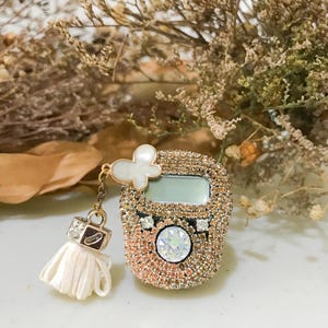 May include: A decorative digital counter with a rose gold finish, encrusted with sparkling crystals. It features a white butterfly charm and a small tassel. The counter has a small screen and a central, large crystal.