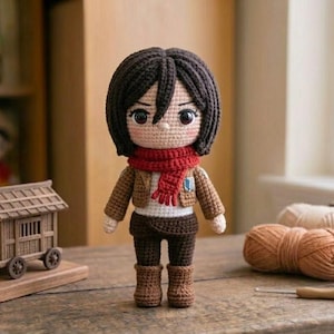 Puede incluir: Muñeca de ganchillo hecha a mano de un personaje con cabello oscuro, una bufanda roja y una chaqueta marrón. La muñeca está sobre una superficie de madera, con una pequeña casa de madera sobre ruedas y lana en el fondo.