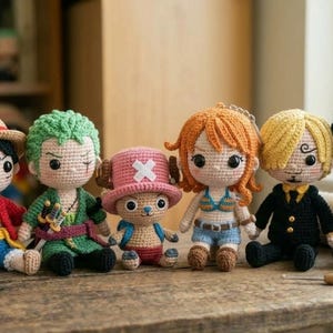 Puede incluir: Una colección de siete muñecos de ganchillo, cada uno representando a un personaje de una popular serie de anime. Los muñecos presentan peinados, atuendos y accesorios distintivos, incluido un barco pirata. Están colocados sobre una superficie de madera.
