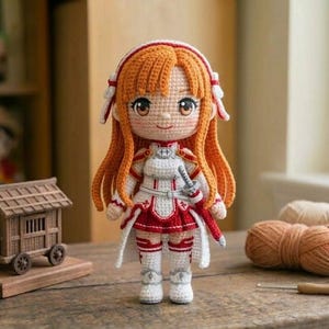 Puede incluir: Muñeca de ganchillo hecha a mano con cabello naranja, vestida con un atuendo blanco y rojo con una espada. La muñeca tiene ojos marrones grandes y está sobre una superficie de madera. Otros artículos de ganchillo y una casa de madera en miniatura están en el fondo.