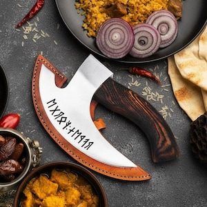May include: A handcrafted axe with a polished steel blade and a dark wood handle. The blade has etched text and is set in a leather sheath. The axe is displayed with food items, including rice, onions, and spices.