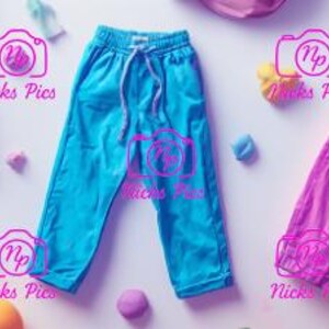 May include: An overhead shot of colorful drawstring pants in shades of blue, purple, and pink. The pants are arranged with small toys and other objects on a white background. The image has a playful and vibrant aesthetic.