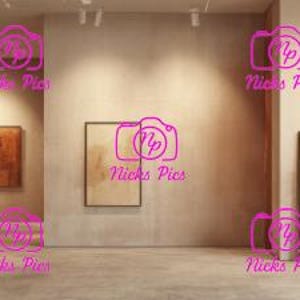 May include: An art gallery interior featuring multiple framed paintings displayed on neutral-colored walls. The artwork varies in style and color, with warm lighting illuminating the space. The gallery floor is a light gray color.
