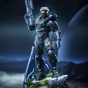 May include: A detailed collectible figurine of a soldier in green and grey tactical armor with a gold visor, holding a futuristic rifle. The figure stands on a rocky base with blue glowing accents and green foliage, featuring the text Tanuki Figures.