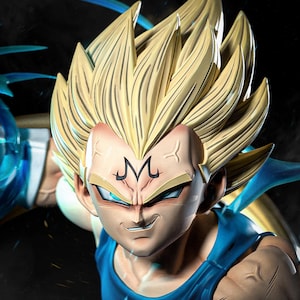 May include: A detailed figure of a character with spiky blonde hair and a determined expression. The figure wears a blue outfit and has a distinctive 'M' symbol on its forehead. The Tanuki Figures logo is visible, along with a call to action: 'AVAILABLE ON PATREON'.